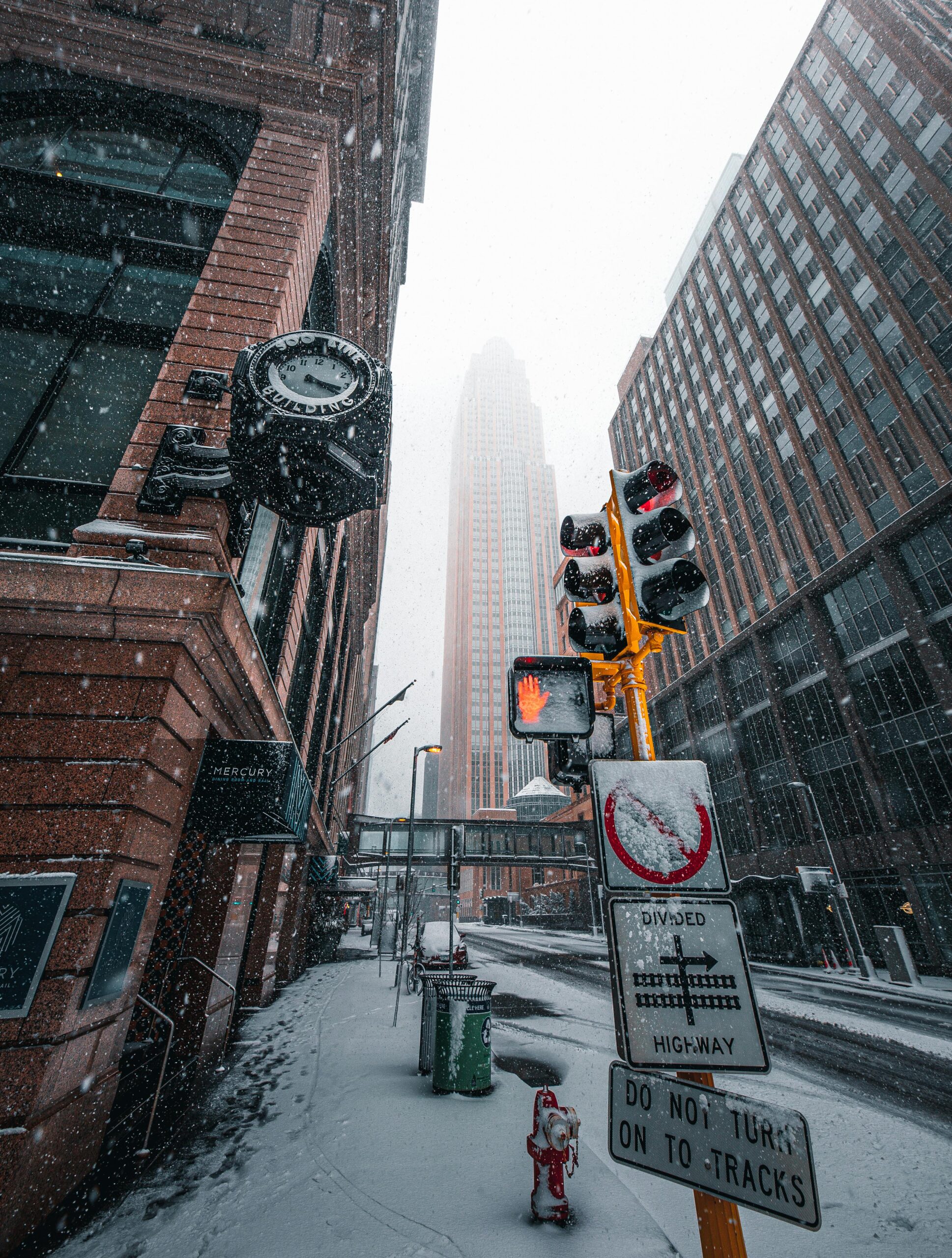 Urban winter scene with snow-covered street in downtown Minneapolis, featuring highrise buildings and traffic lights.