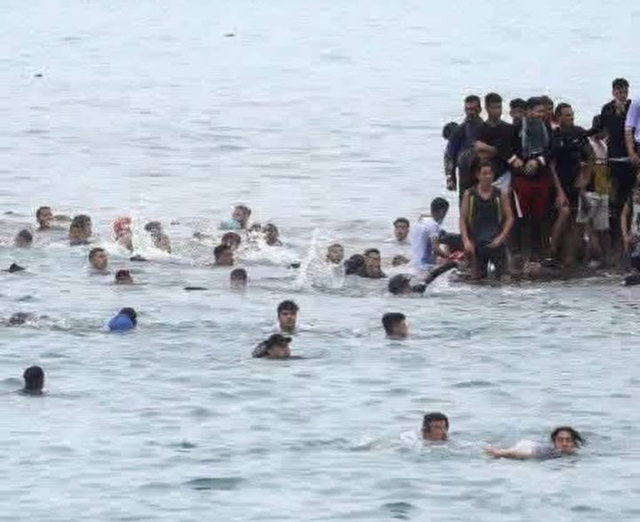 Migrants arriving near the Ceuta coastline under emergency response.